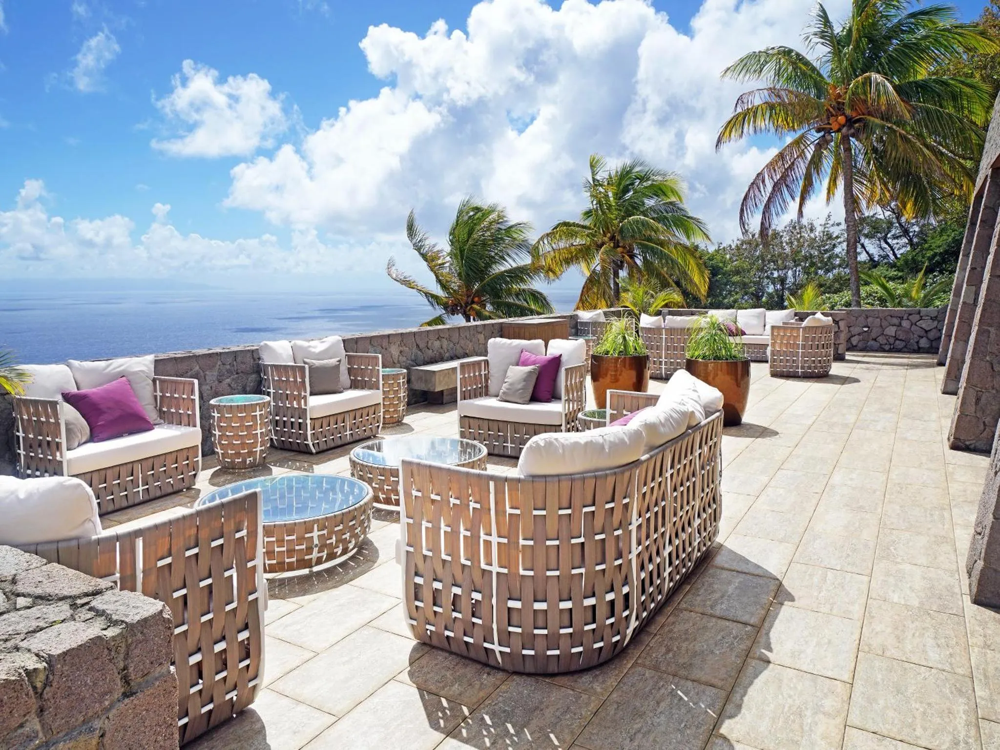 Espace de détente extérieur avec mobilier en rotin et vue sur la mer.
