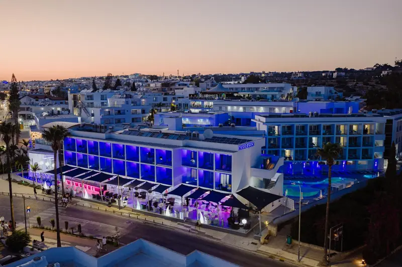 Bâtiment moderne illuminé au crépuscule avec des palmiers et une piscine.