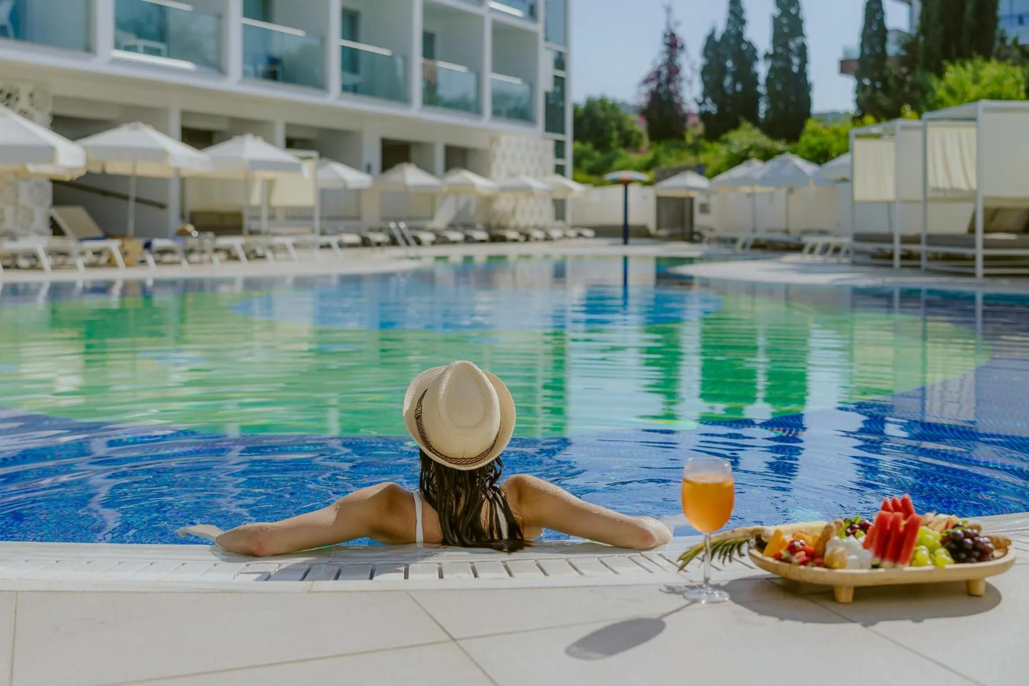 Une personne se détend au bord d'une piscine avec une boisson et des fruits.