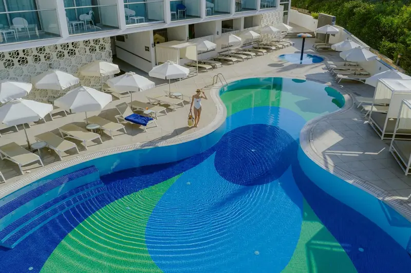 Vue aérienne d'une piscine sinueuse avec des transats et parasols.