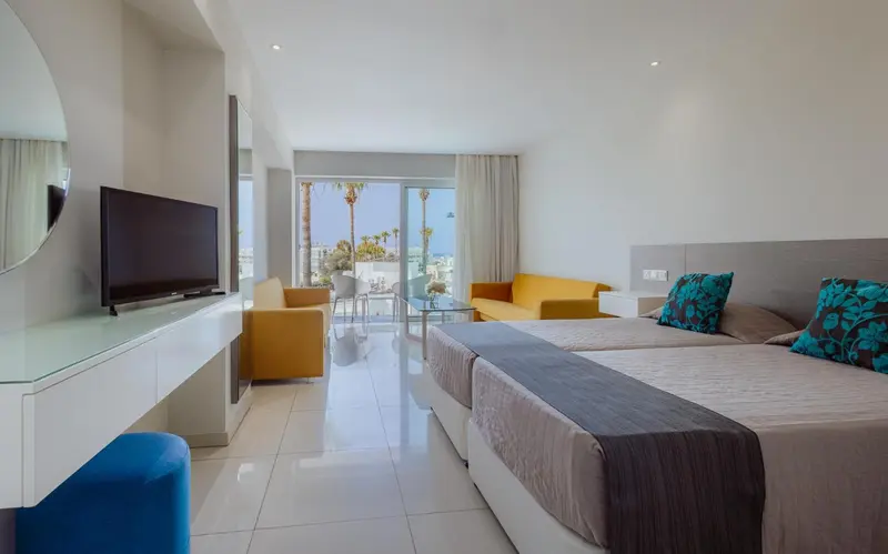 Une chambre lumineuse avec un lit double et un coin salon donnant sur une vue extérieure.