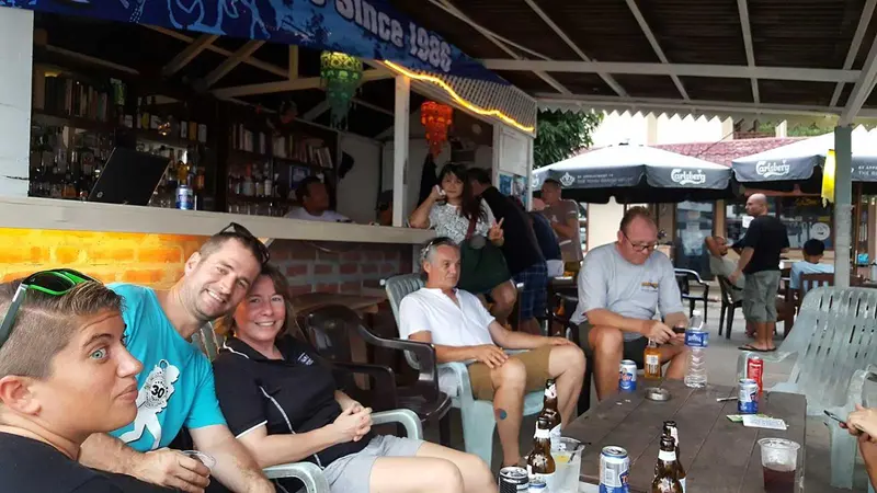 Un bar en plein air avec des clients assis au comptoir et sur des chaises en plastique.