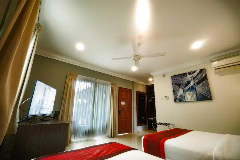 Une chambre lumineuse avec un lit recouvert d'une courtepointe rouge et un téléviseur fixé au mur.