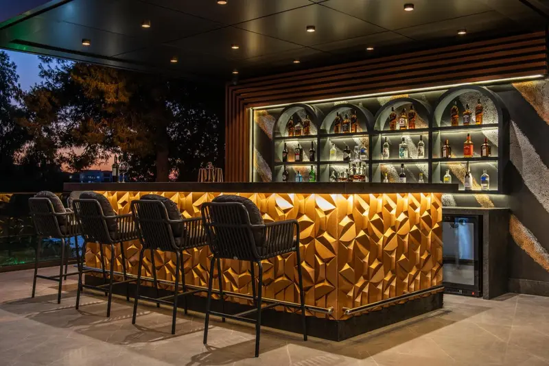 Un bar extérieur illuminé avec des tabourets et une sélection de boissons.