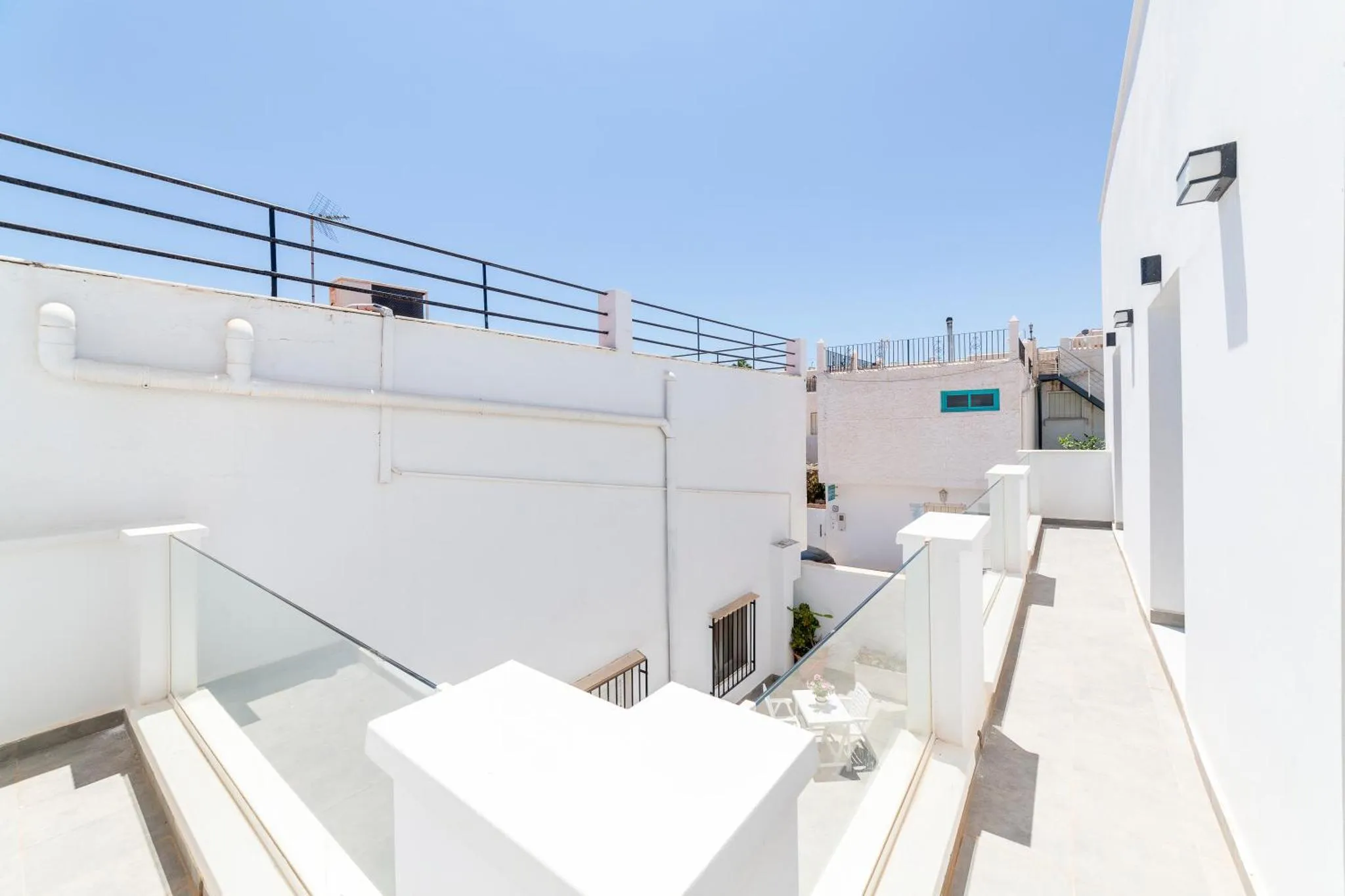 Terrasse blanche avec garde-corps en verre et escalier.
