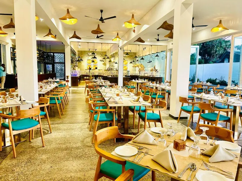 Une salle de restaurant lumineuse avec des tables dressées et des chaises turquoise.