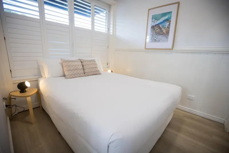 Une chambre lumineuse avec un lit recouvert de draps blancs et une décoration minimaliste.