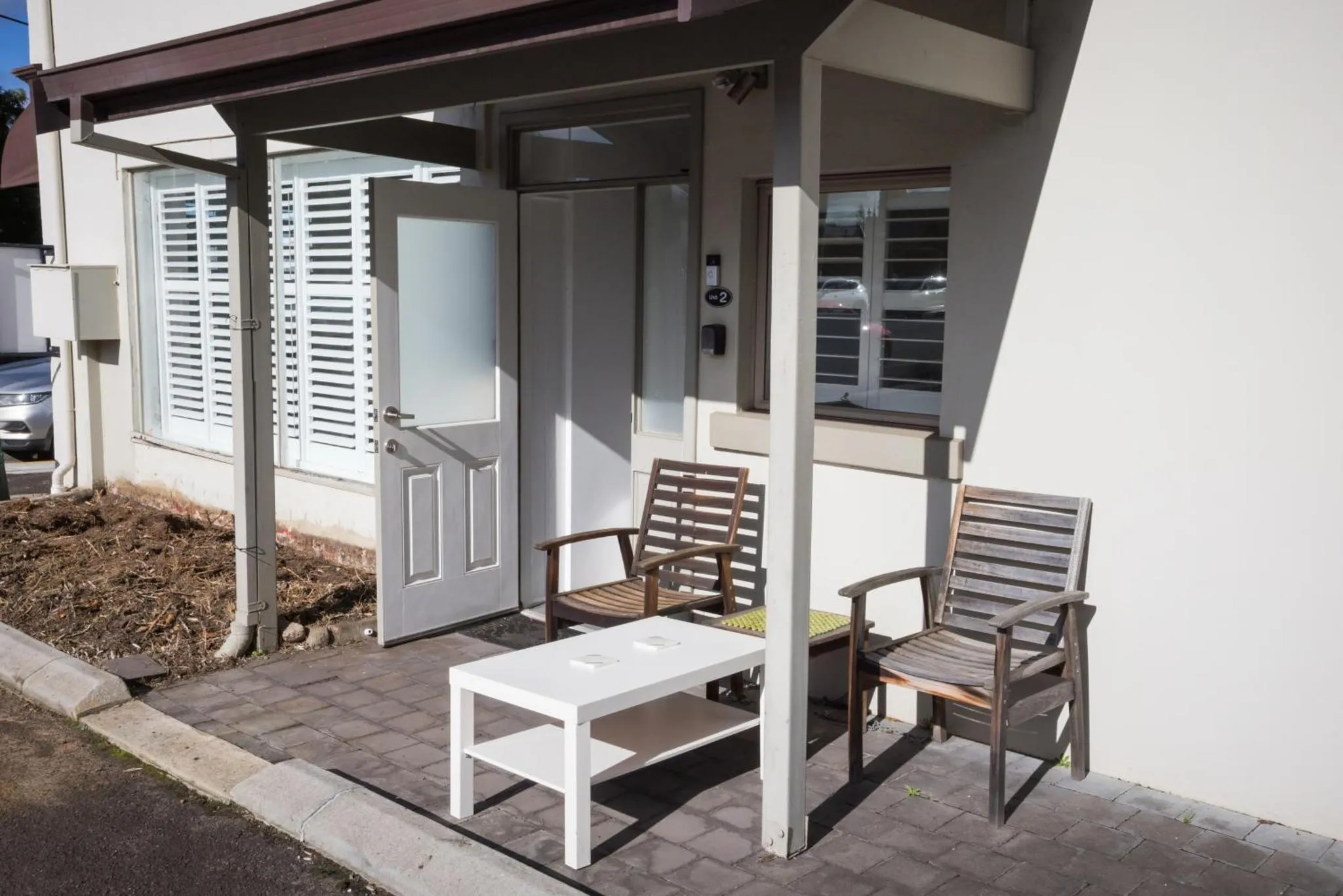 Une terrasse avec deux fauteuils et une petite table basse devant une porte d'entrée.