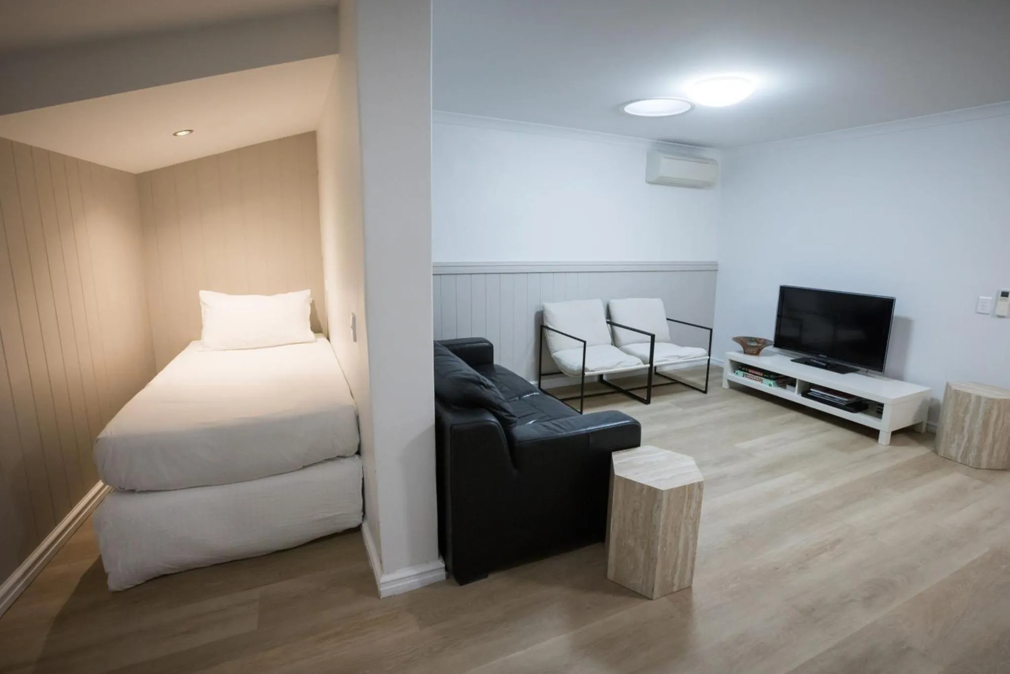 Une pièce lumineuse combine un espace de repos avec un lit simple et un coin salon avec canapé et télévision.