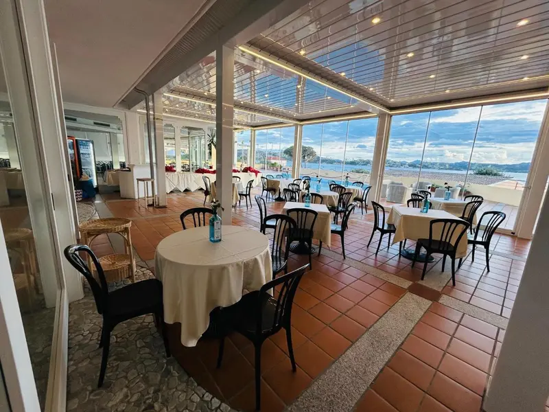 Une salle lumineuse avec des tables et des chaises donnant sur une vue mer.