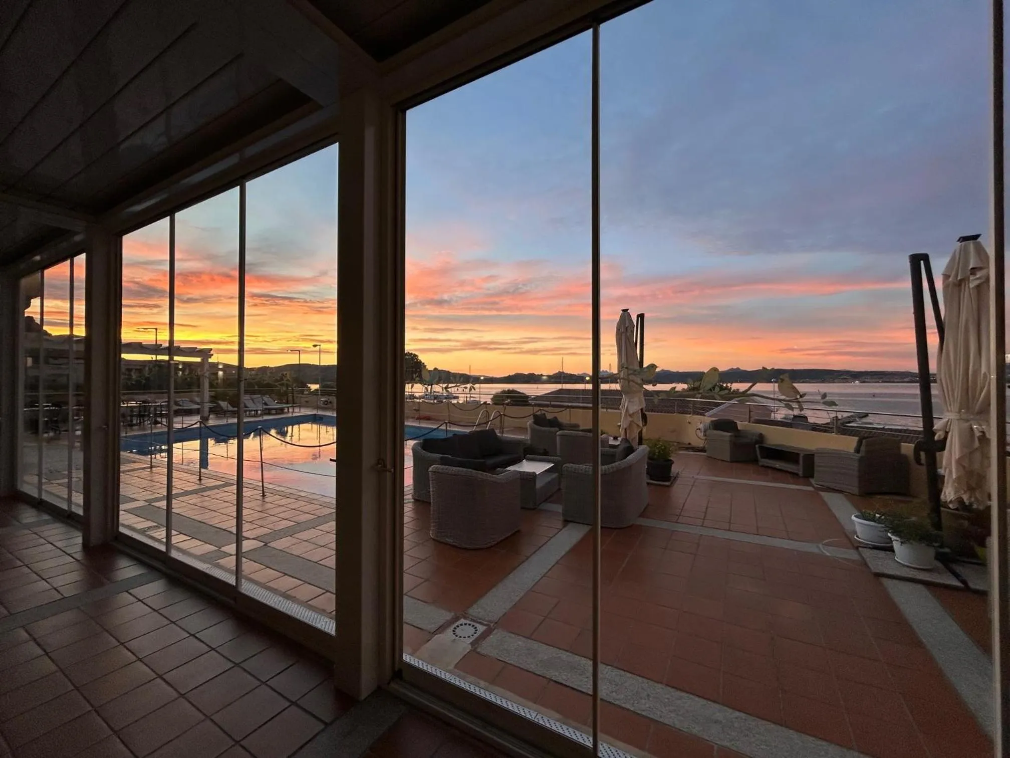 Terrasse carrelée avec mobilier de détente et vue sur la mer au coucher du soleil.