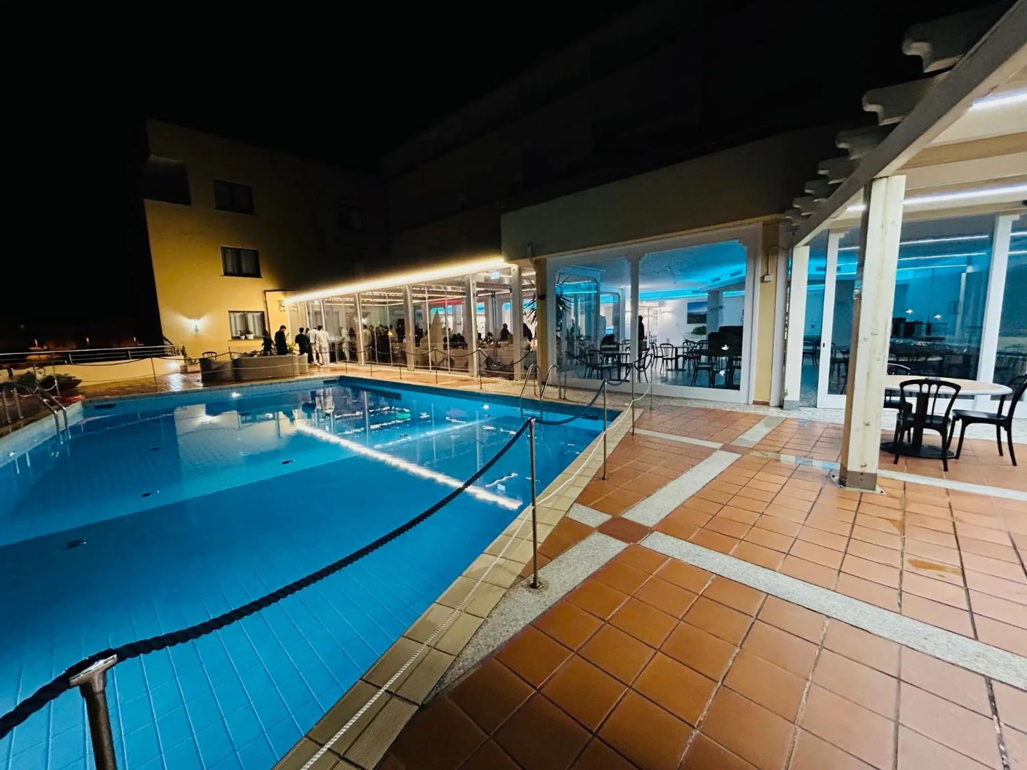 Une piscine illuminée avec des transats et des tables à proximité d'un bâtiment.