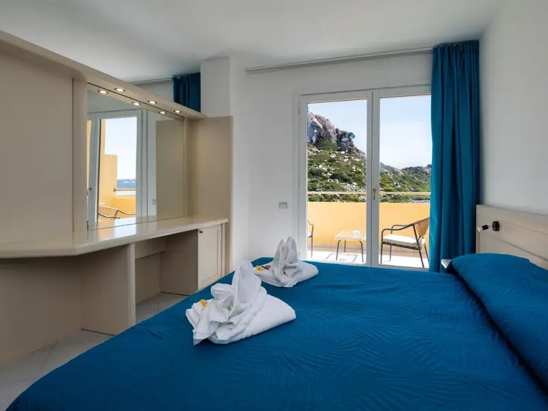 Une chambre lumineuse avec un lit fait et un balcon offrant une vue sur la mer.