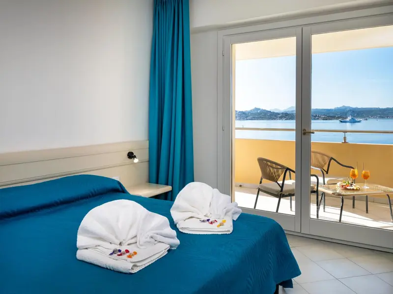 Une chambre lumineuse avec un lit fait et un accès à une terrasse vue sur mer.