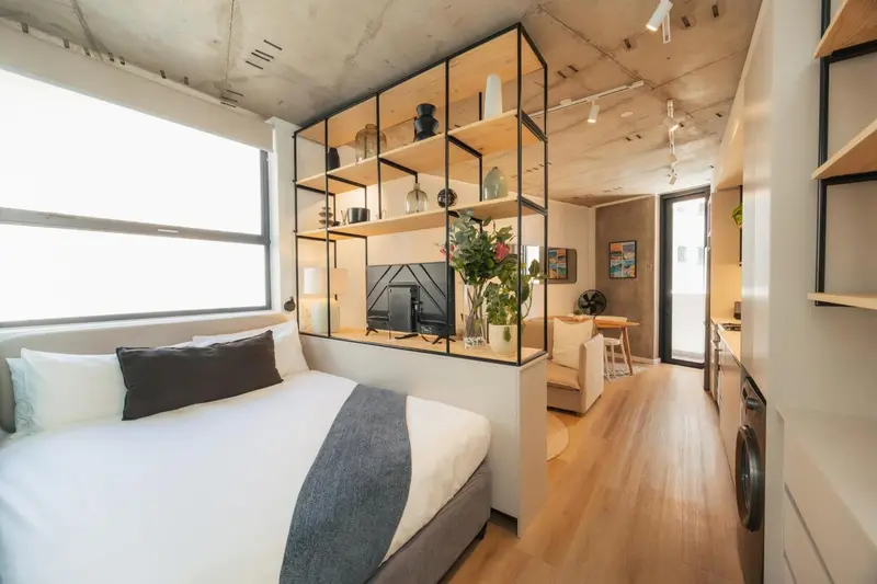 Intérieur lumineux avec un lit fait et une étagère ouverte.