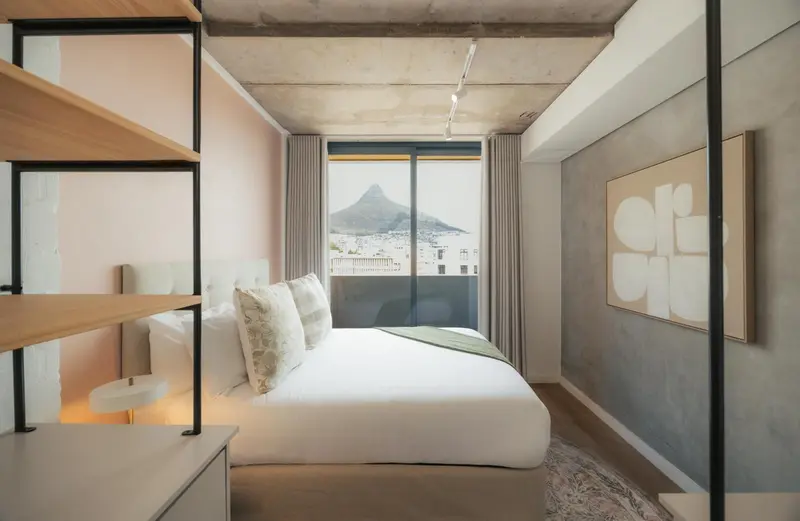 Chambre lumineuse avec un grand lit et une vue sur la ville.