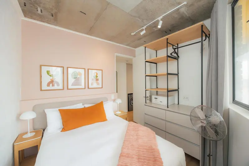 Une chambre lumineuse avec un lit recouvert d'une couverture orange et des tableaux décoratifs.