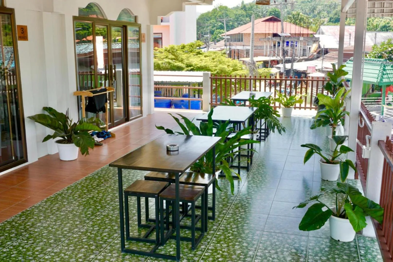 Terrasse carrelée avec tables et chaises en bois sombre, agrémentée de plantes vertes.