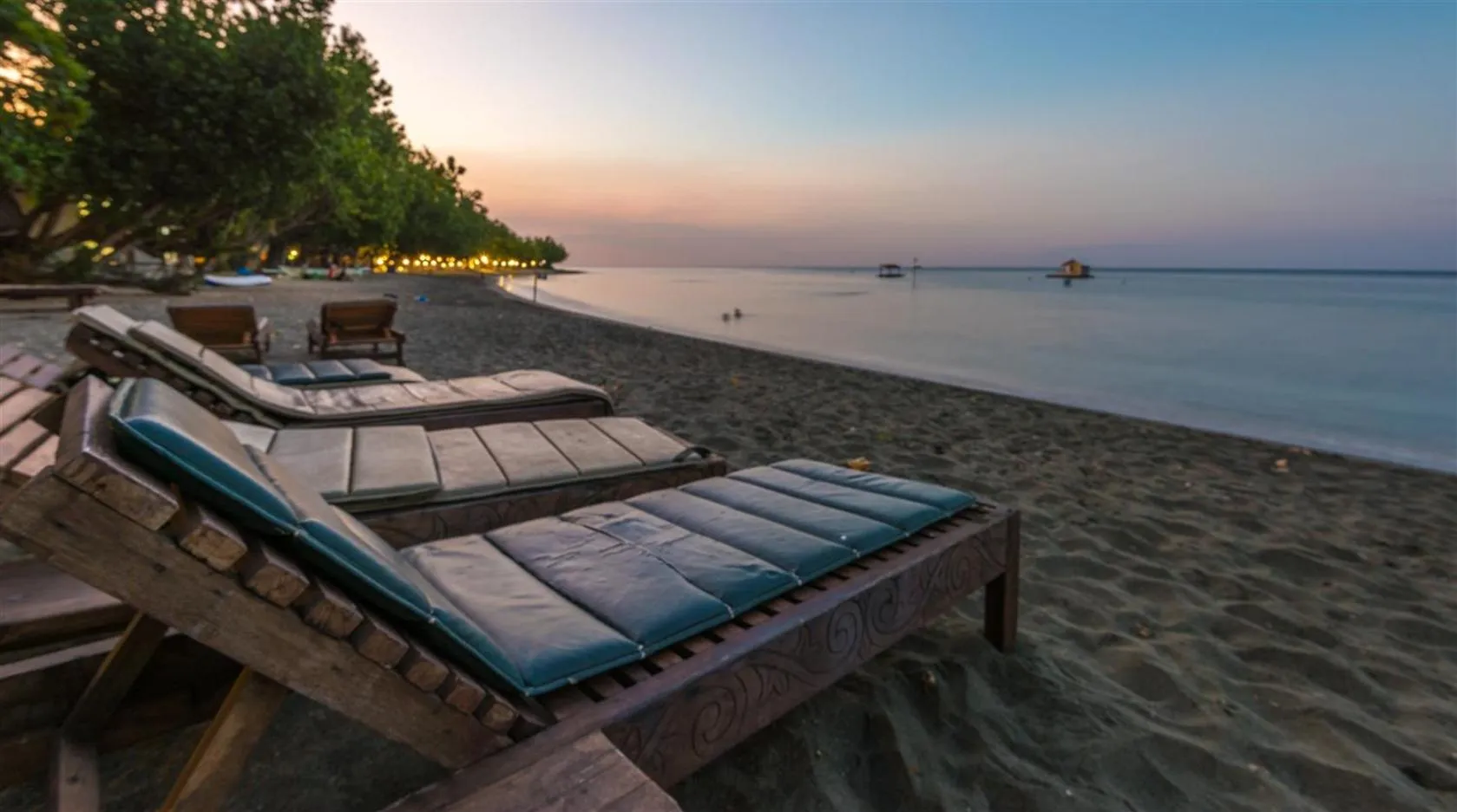 Transats alignés sur une plage de sable sombre au coucher du soleil.