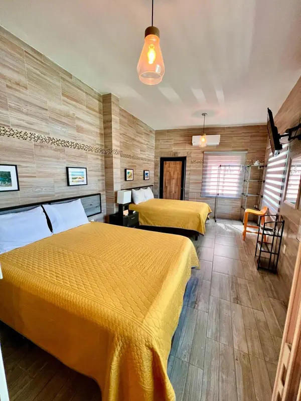 Chambre avec deux lits simples recouverts d'une courtepointe jaune et un éclairage suspendu.