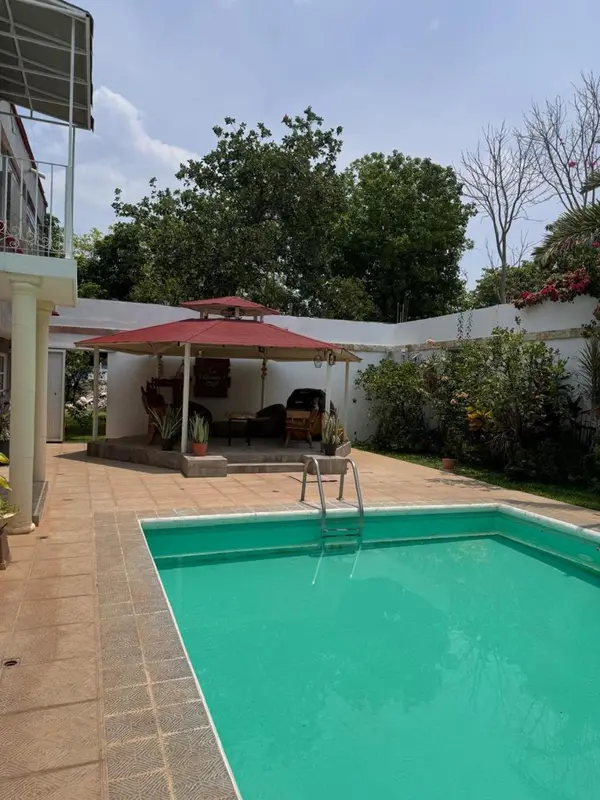 Une piscine turquoise avec un espace de détente ombragé à proximité.