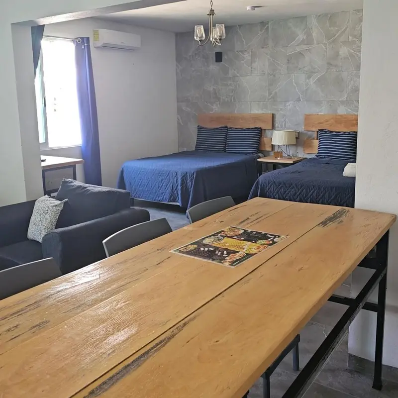 Une table en bois est placée devant deux lits simples dans une pièce lumineuse.