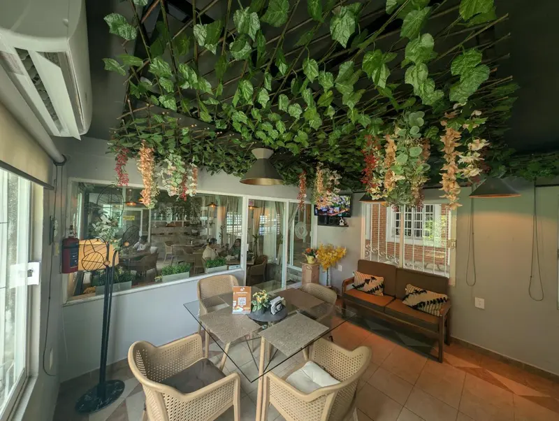 Espace de détente intérieur avec tables et canapés sous une décoration végétale suspendue.