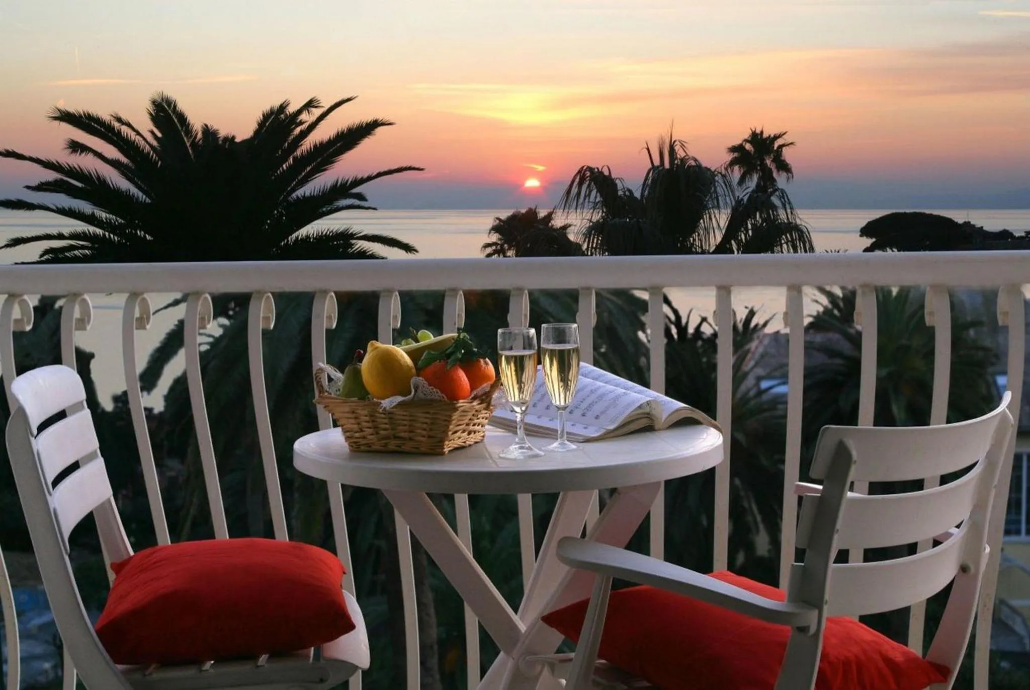 Une table avec des fruits et des verres sur une terrasse face à la mer au coucher du soleil.