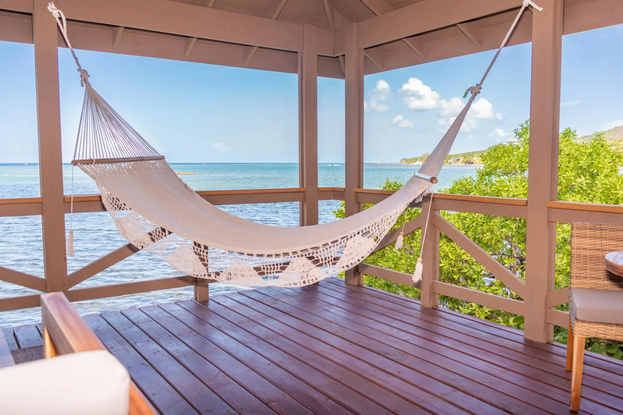 Un hamac blanc est suspendu sur une terrasse en bois avec vue sur la mer.
