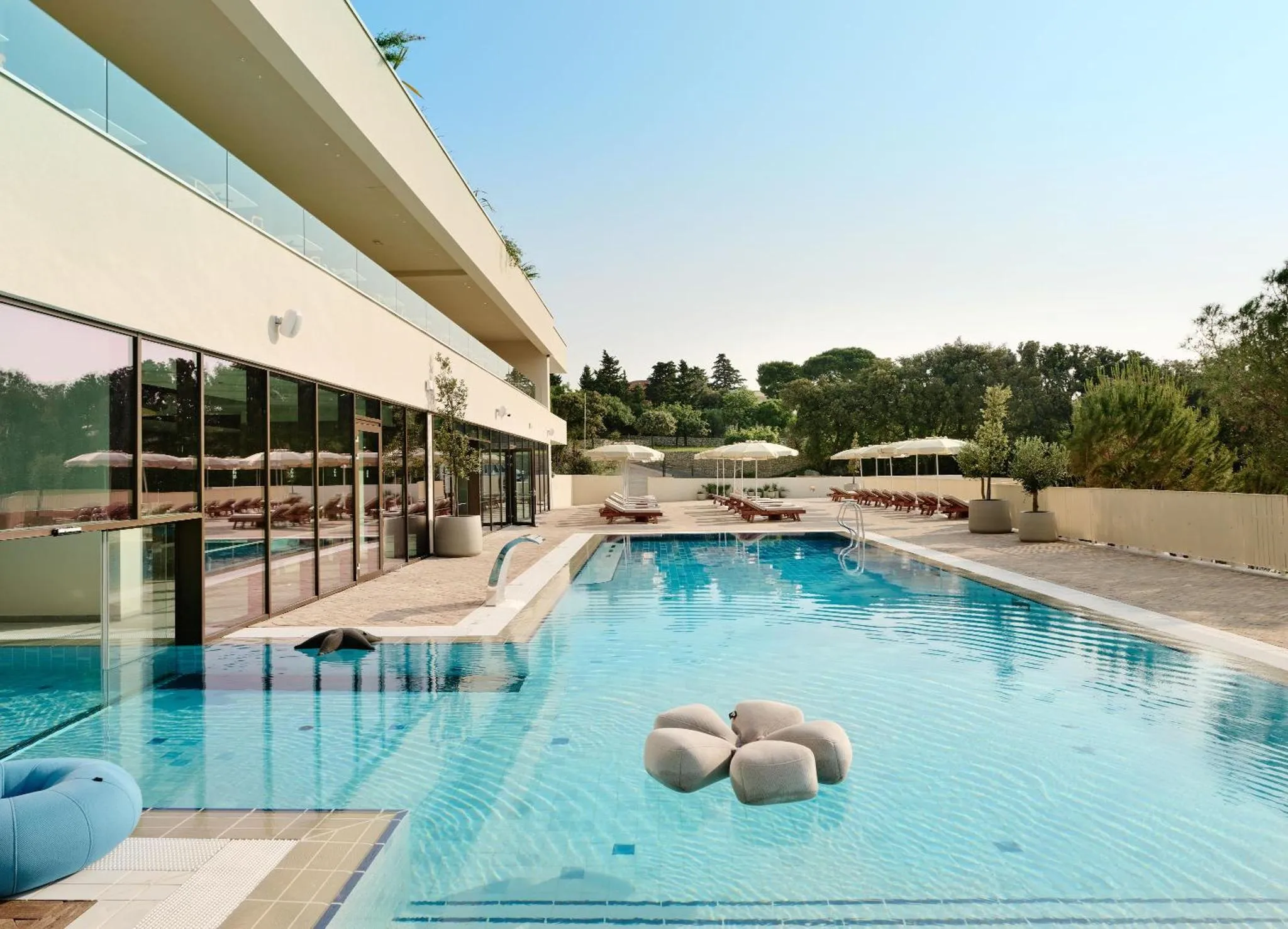 Une piscine rectangulaire bleu clair avec des transats et des parasols sur une terrasse ensoleillée.