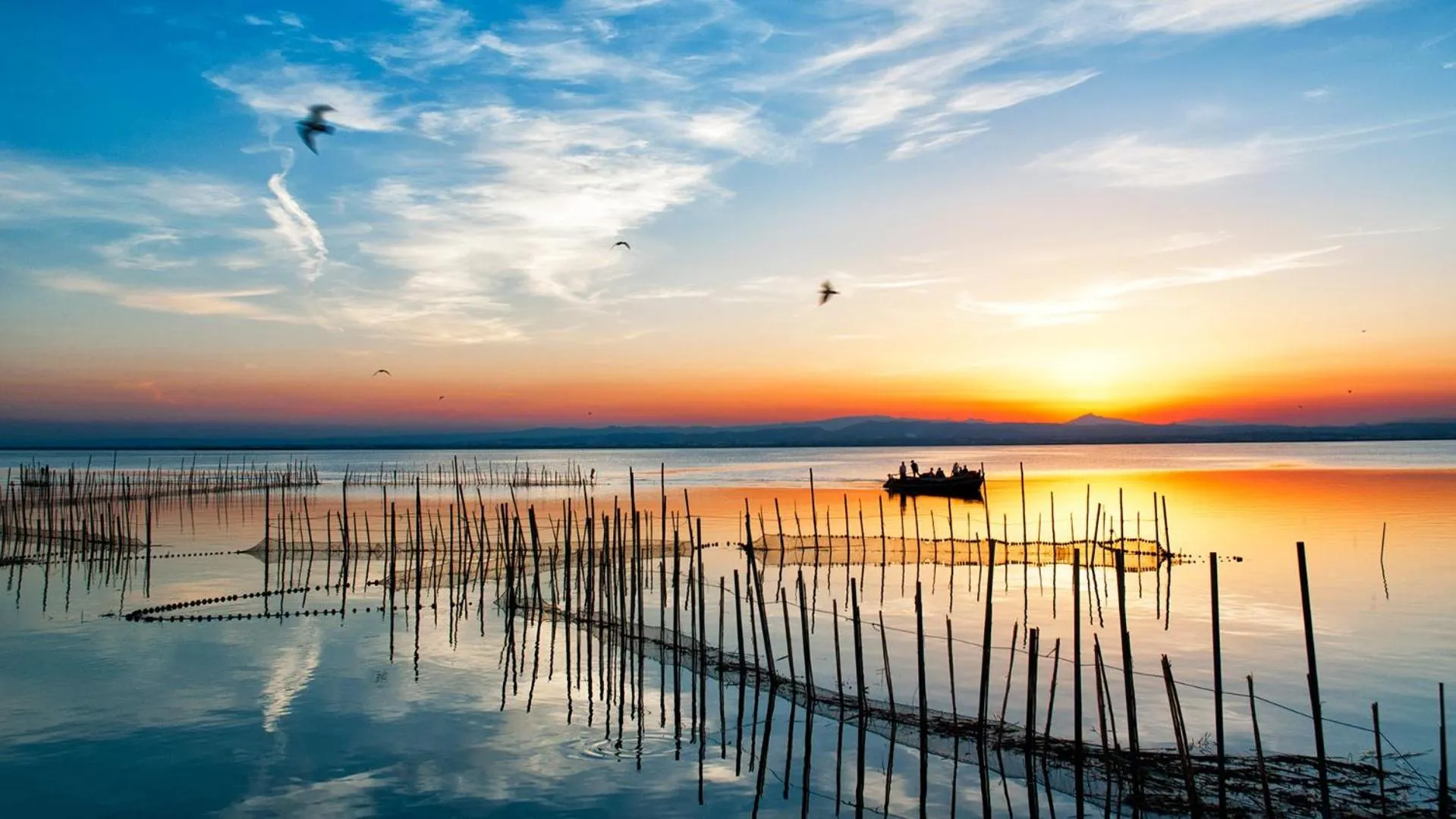 Coucher de soleil sur une étendue d'eau calme avec des pieux en bois et un petit bateau.