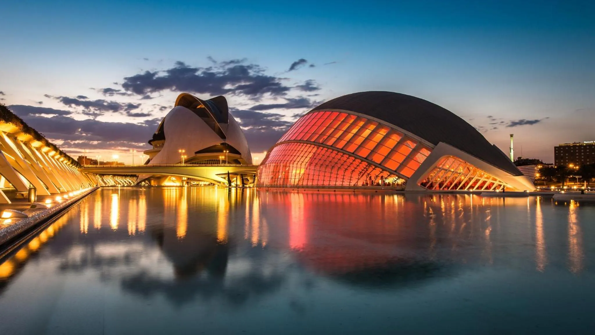 Architecture moderne illuminée se reflétant dans une étendue d'eau calme au crépuscule.