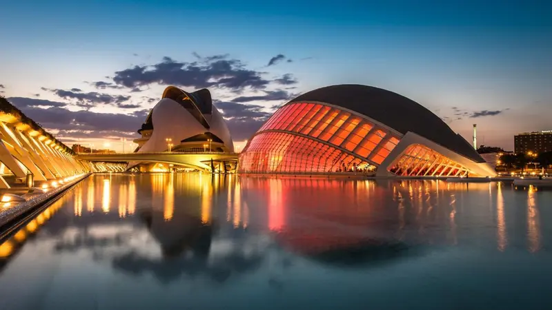 Architecture moderne illuminée se reflétant dans une étendue d'eau calme au crépuscule.