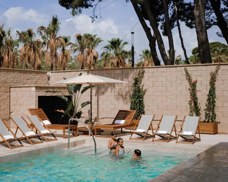 Des transats sont disposés autour d'une piscine où des enfants jouent.