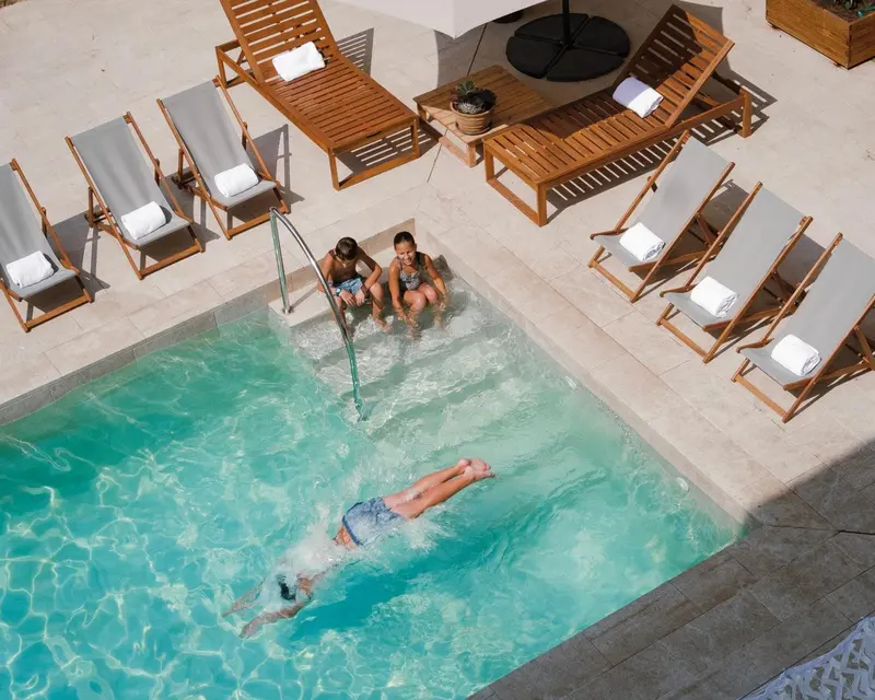 Transats alignés autour d'une piscine rectangulaire où nagent des personnes.