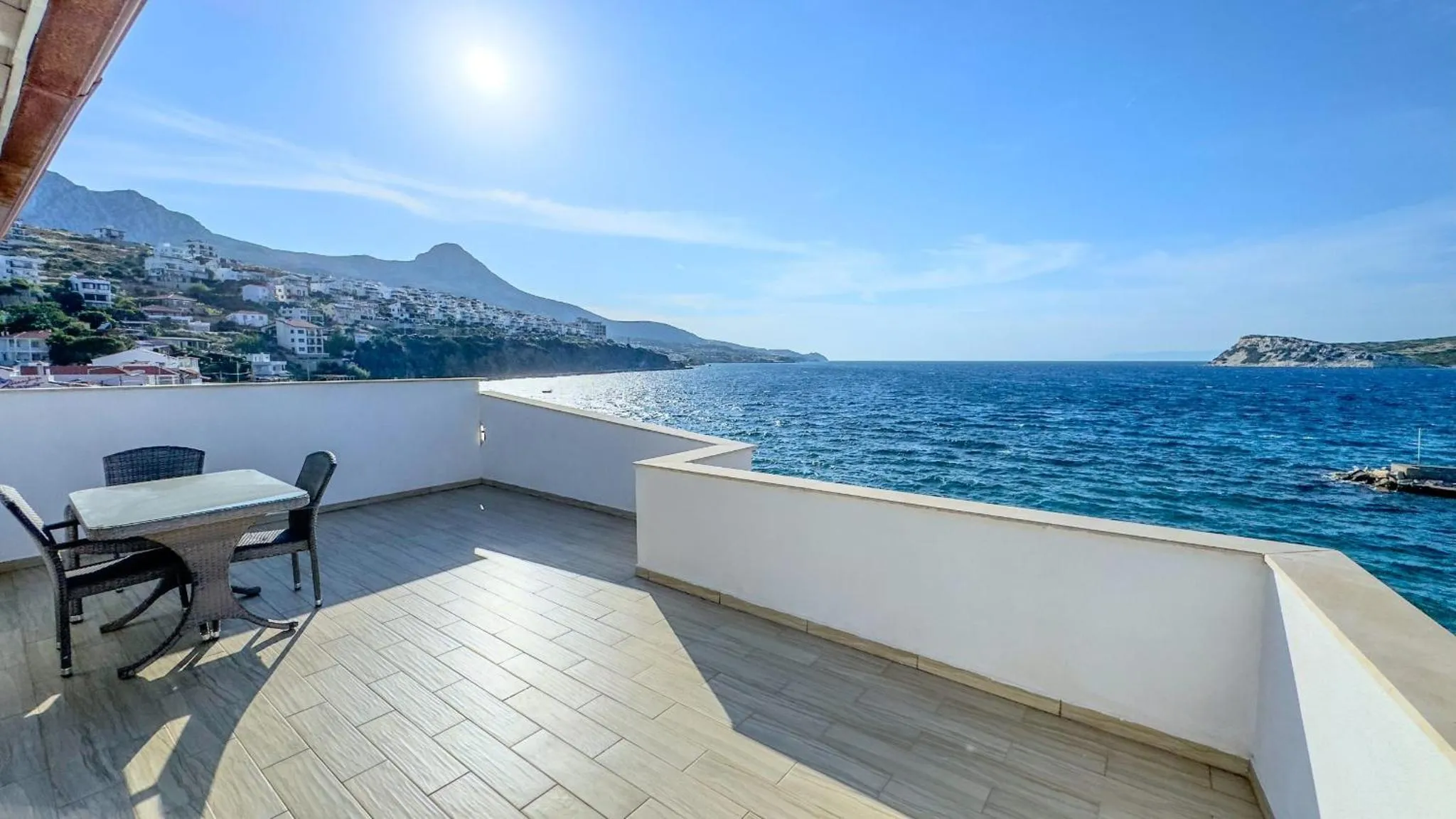 Terrasse carrelée avec table et chaises donnant sur la mer et les montagnes.