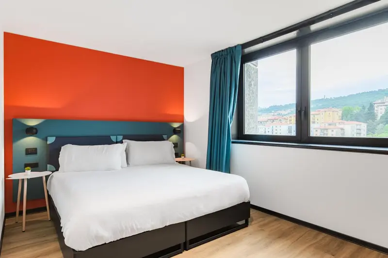 Chambre lumineuse avec un lit double et une vue sur un paysage verdoyant.