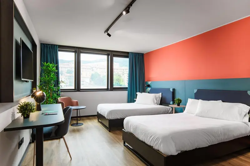 Chambre moderne avec deux lits simples et une vue sur un paysage urbain.