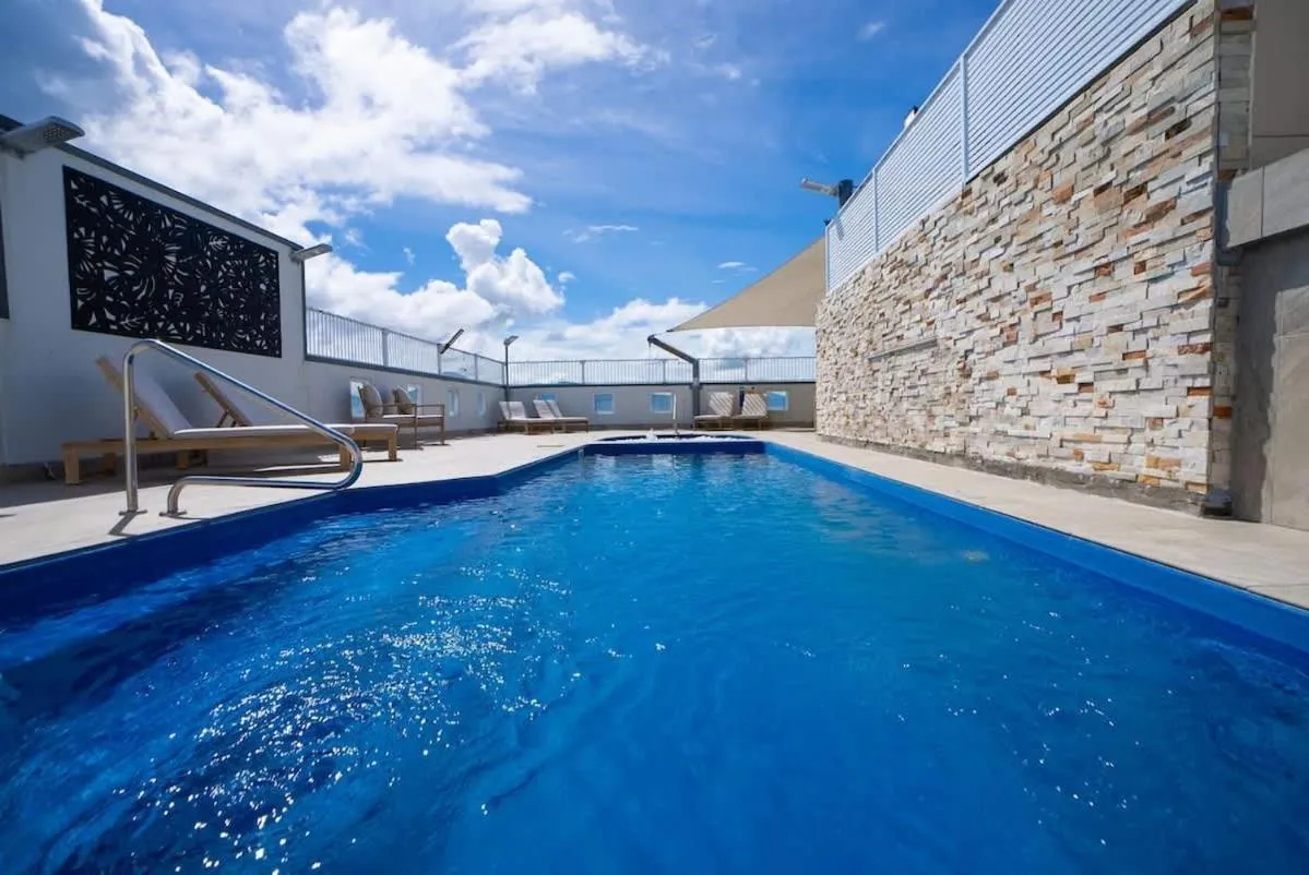 Une piscine rectangulaire bleu clair avec des transats sur une terrasse ensoleillée.