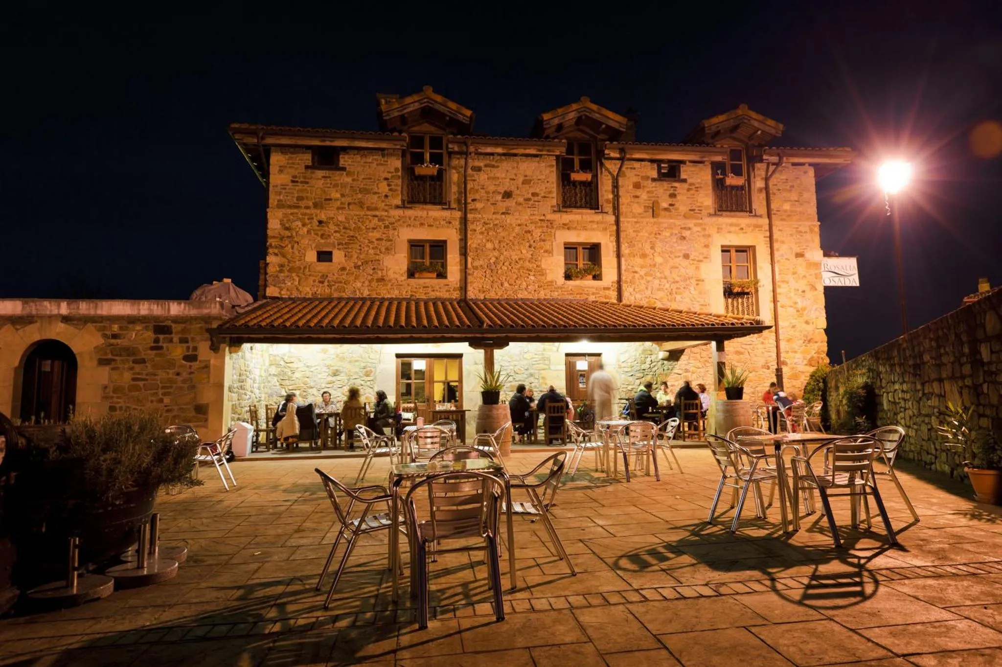 Terrasse éclairée avec tables et chaises devant un bâtiment en pierre.