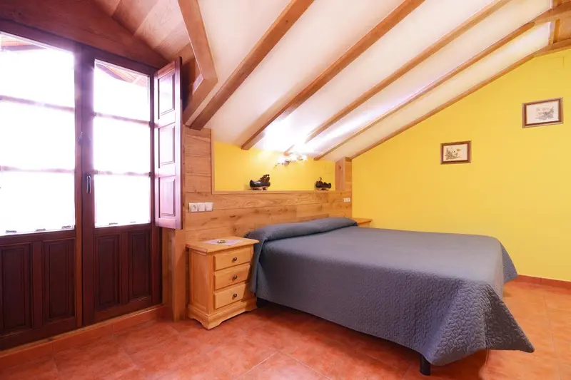 Une chambre mansardée lumineuse avec un lit simple et une fenêtre en bois.