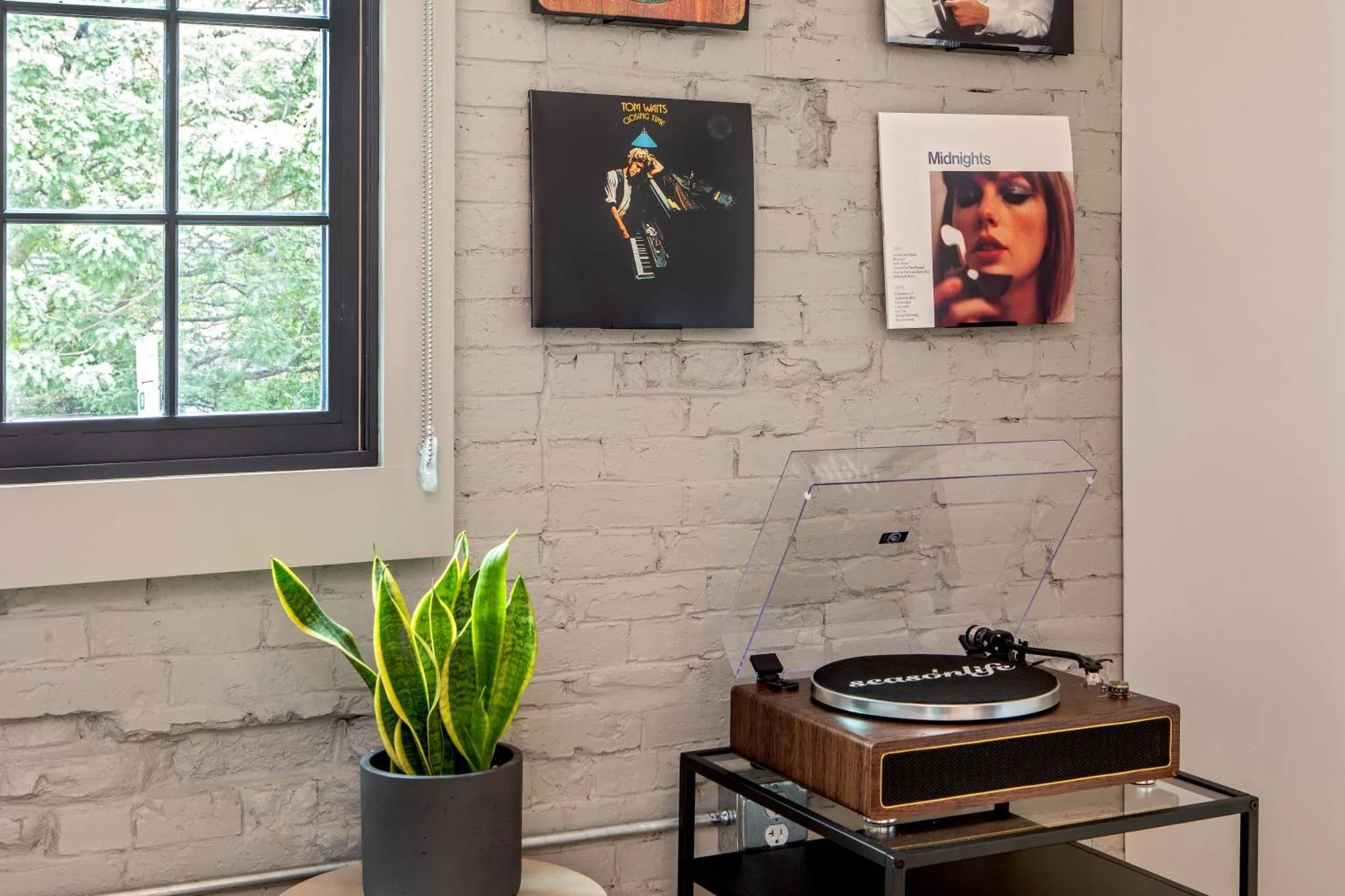 Une platine vinyle repose sur une table basse devant un mur de briques blanches décoré de pochettes de disques.
