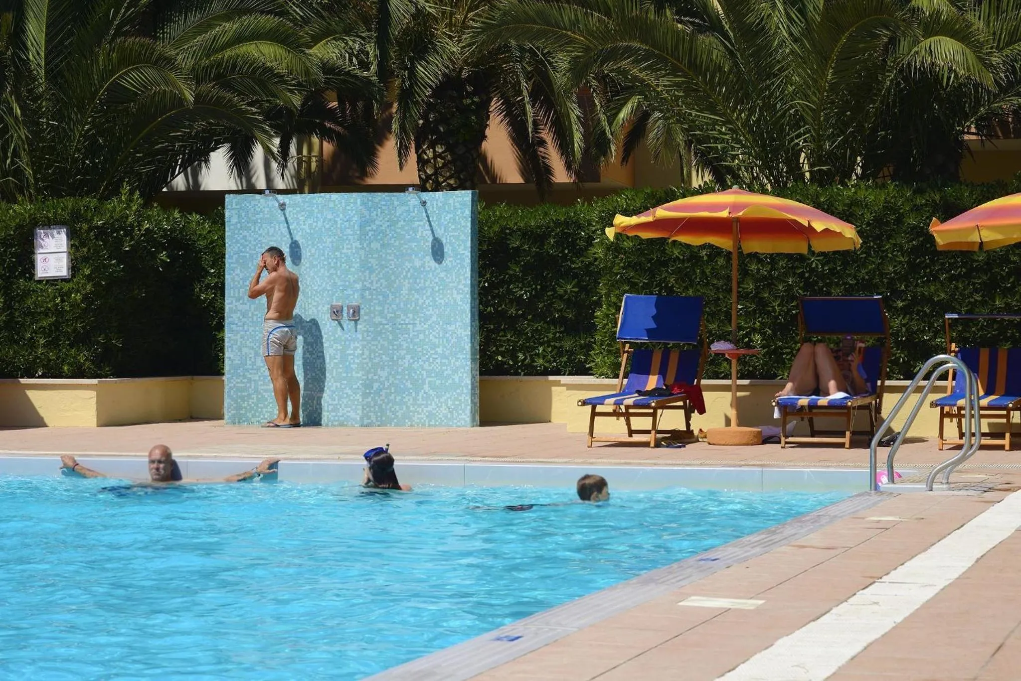 Une personne se rince à la douche près d'une piscine ensoleillée.