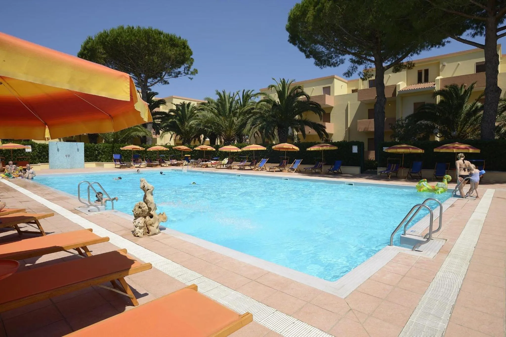Piscine rectangulaire entourée de transats et de palmiers sous le soleil.