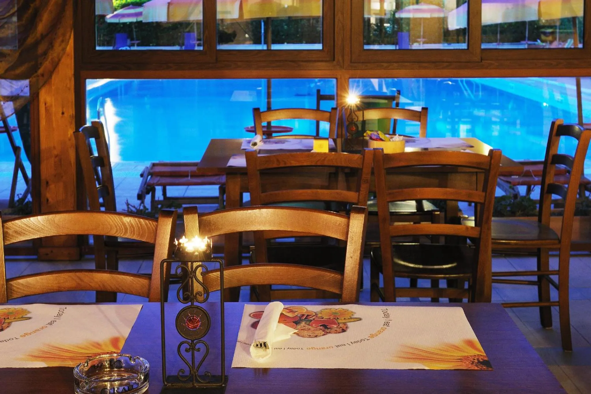 Une salle à manger lumineuse avec des tables dressées près d'une piscine éclairée.