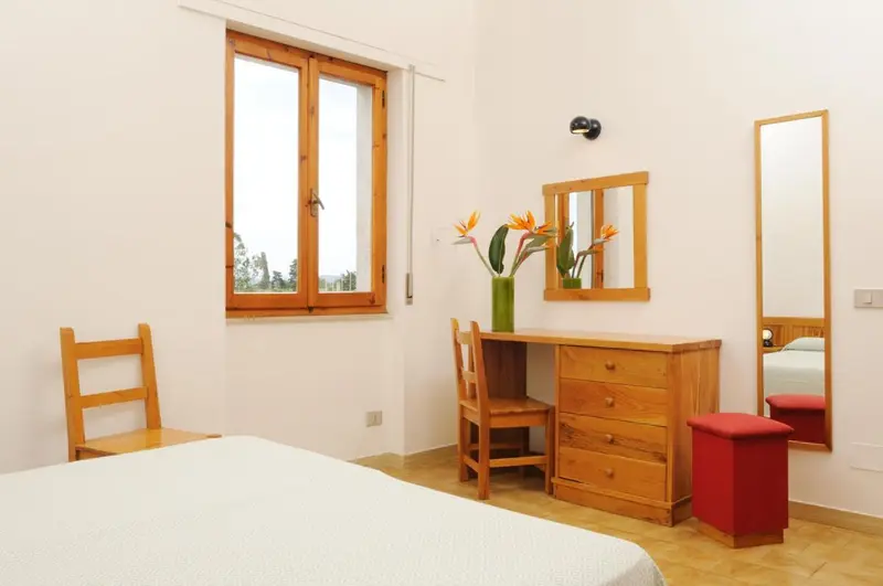 Une chambre lumineuse avec un bureau en bois et un lit recouvert d'un drap blanc.