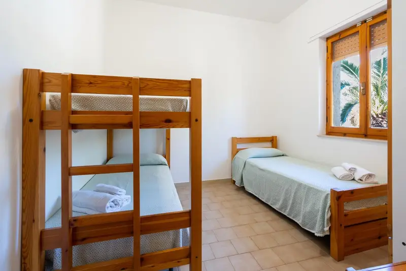 Une chambre avec des lits superposés et un lit simple près d'une fenêtre.