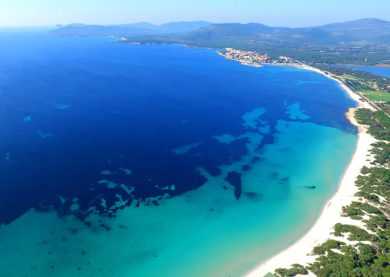 Vue aérienne d'une plage de sable blanc bordée d'une eau turquoise et d'une côte rocheuse.