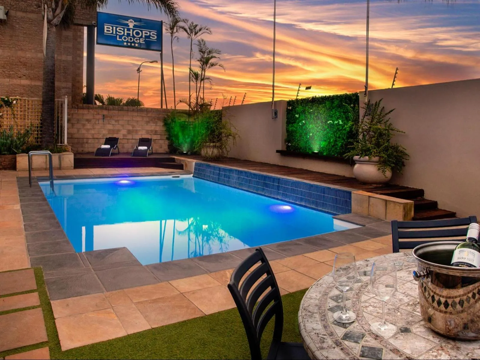Piscine rectangulaire illuminée avec chaises longues et table basse au premier plan.