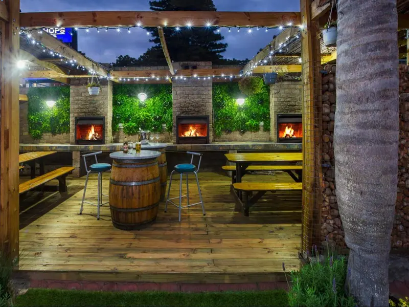 Terrasse boisée avec tables, chaises et foyers illuminés.